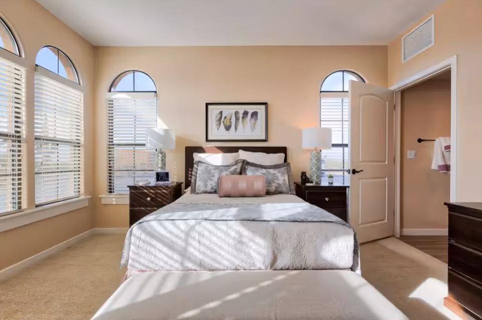 Bright bedroom with arched windows, beige walls, and matching nightstands and lamps.