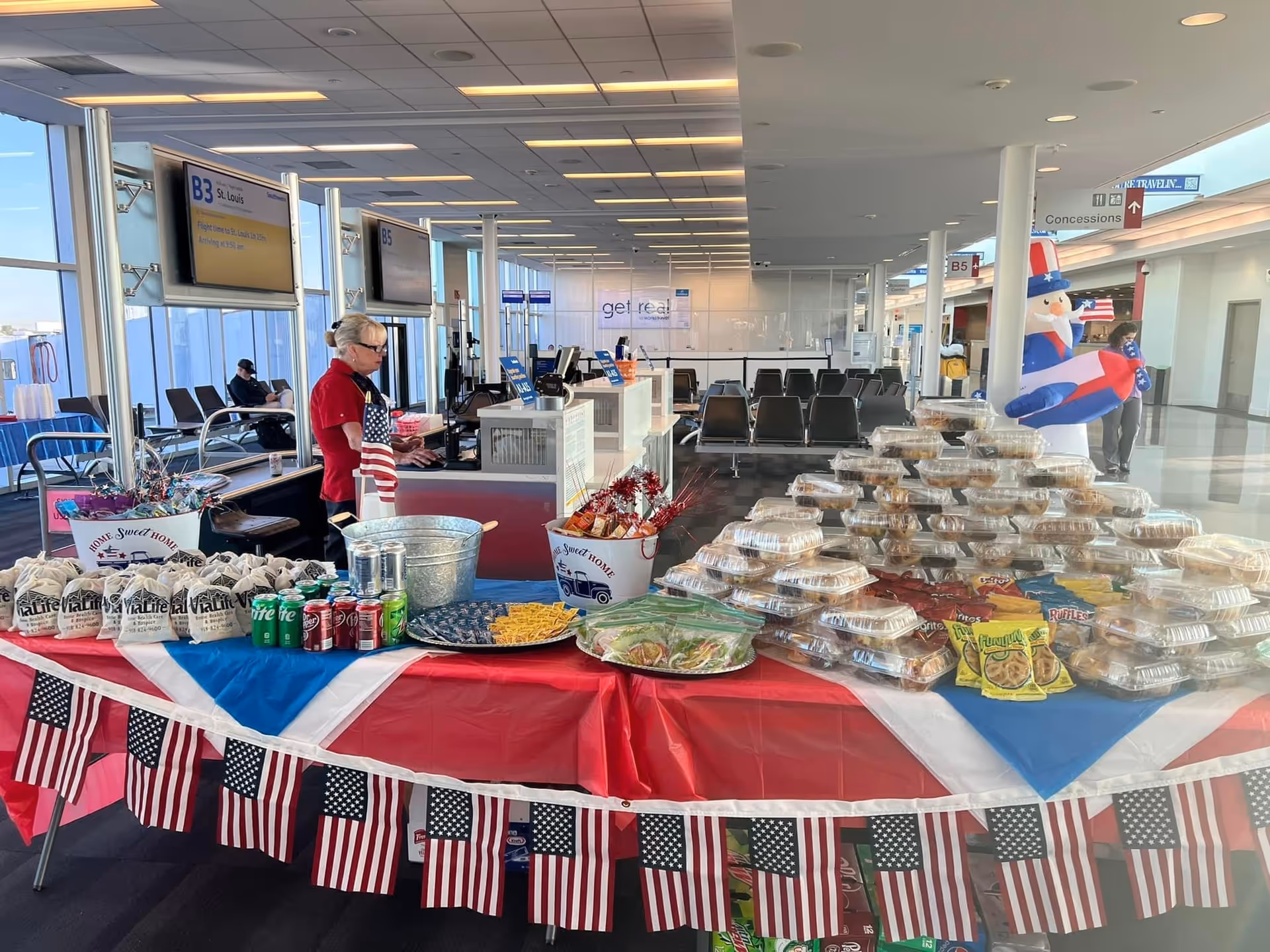Patriotic snack table with cupcakes, drinks, and flags in a bright indoor terminal-like area.