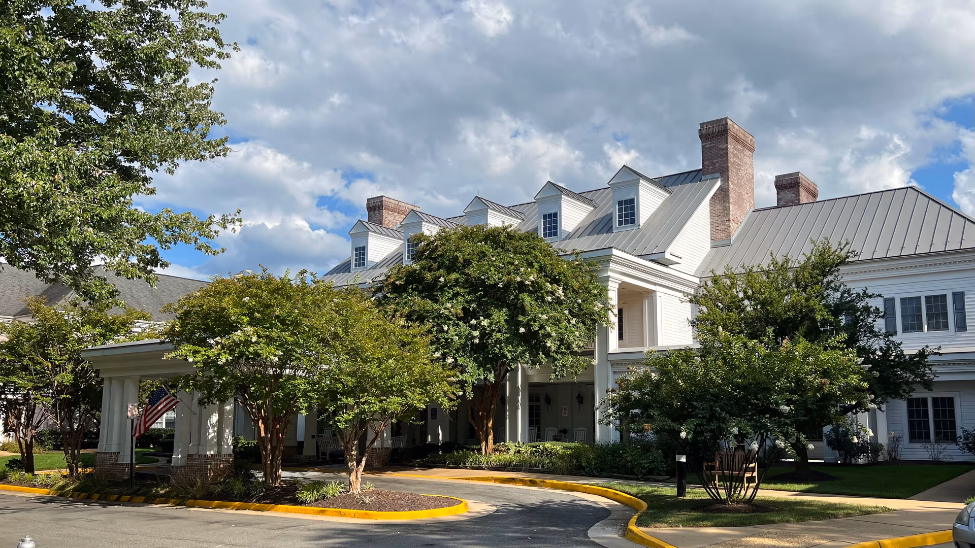 A large white senior living facility exterior with a curved driveway and trees.