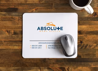 Top-down view of Absolute Home Health branded mousepad on a wooden desk.