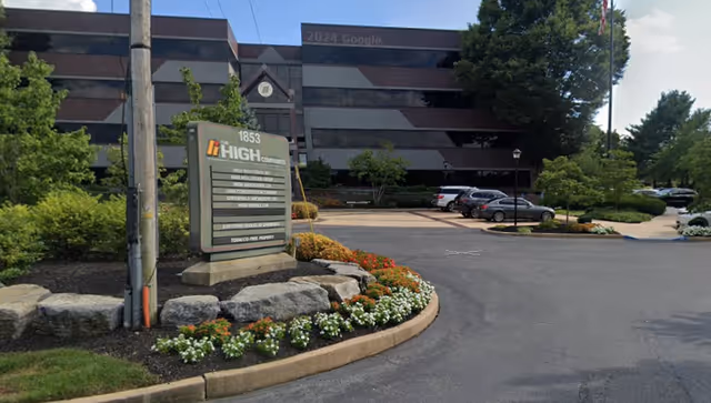 Exterior view of a multi-story building with a landscaped entrance and parked cars.