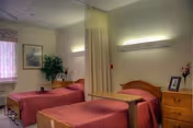 Two twin beds with pink bedspreads and a privacy curtain in a shared patient room.