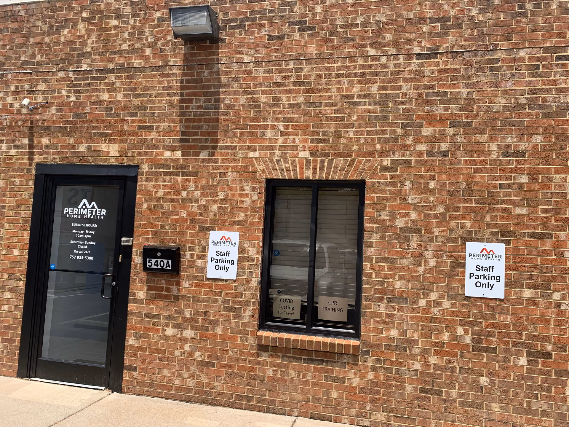 Brick exterior wall with door labeled Perimeter Home Health and staff parking signs.