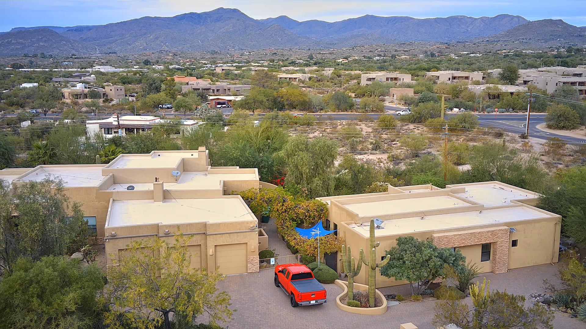 Aerial view of beige southwest-style buildings with desert landscaping, a red pickup in the driveway, and mountains in the background.