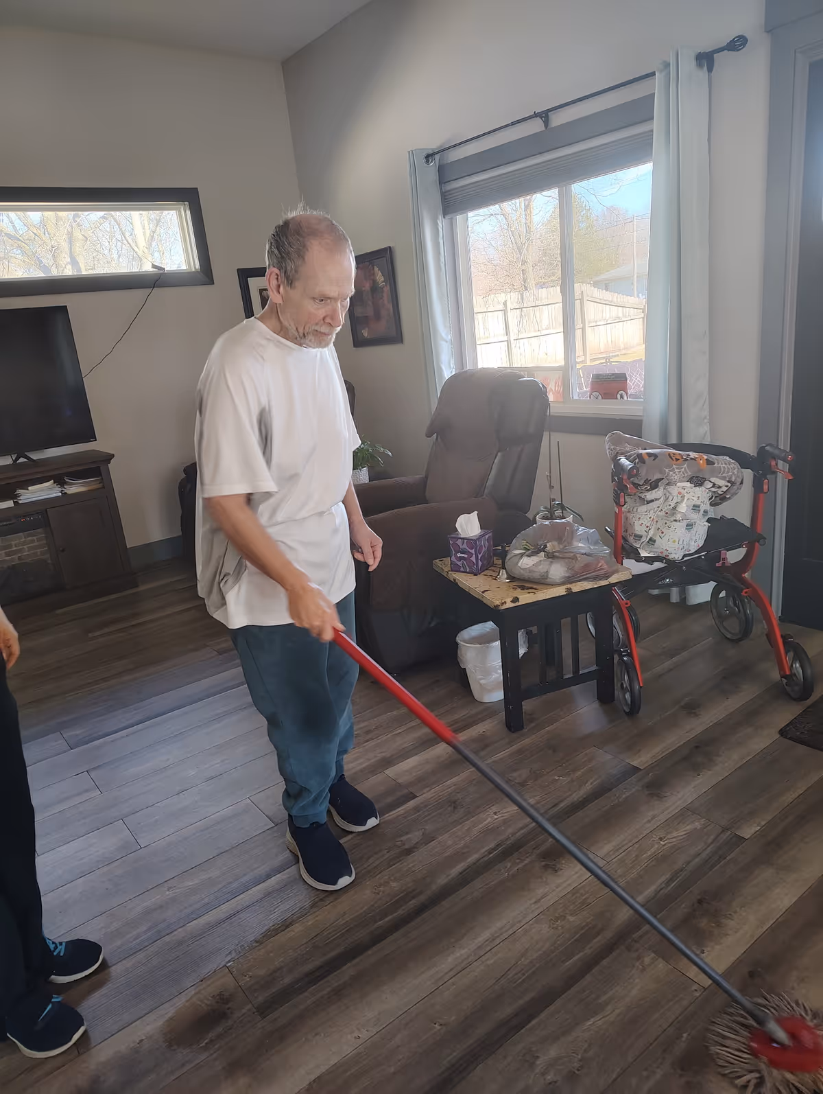 Elderly man mops the living room floor inside a HolistiCare Homes residence