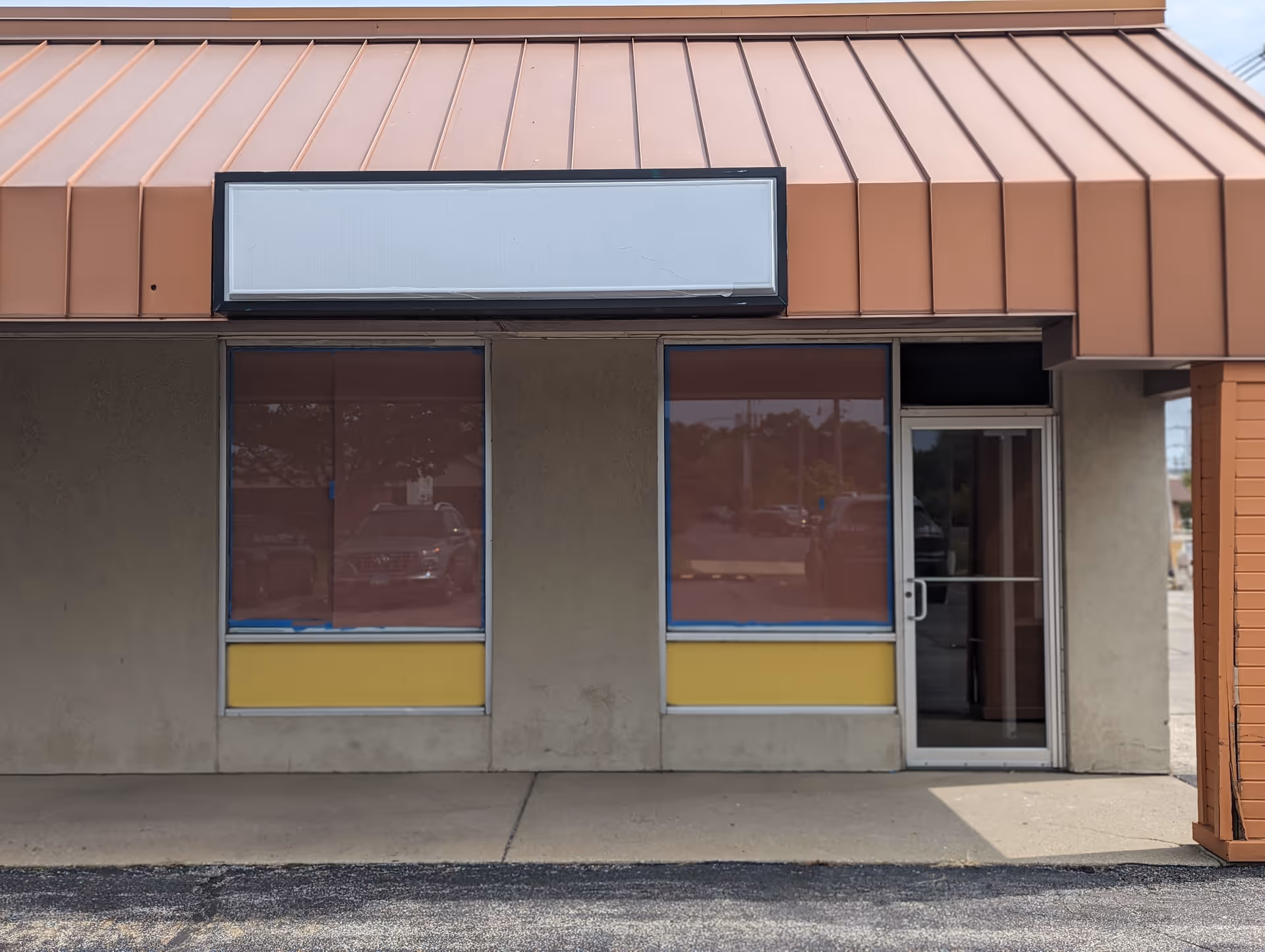 Front of a beige commercial building with a brown metal roof and glass entrance.