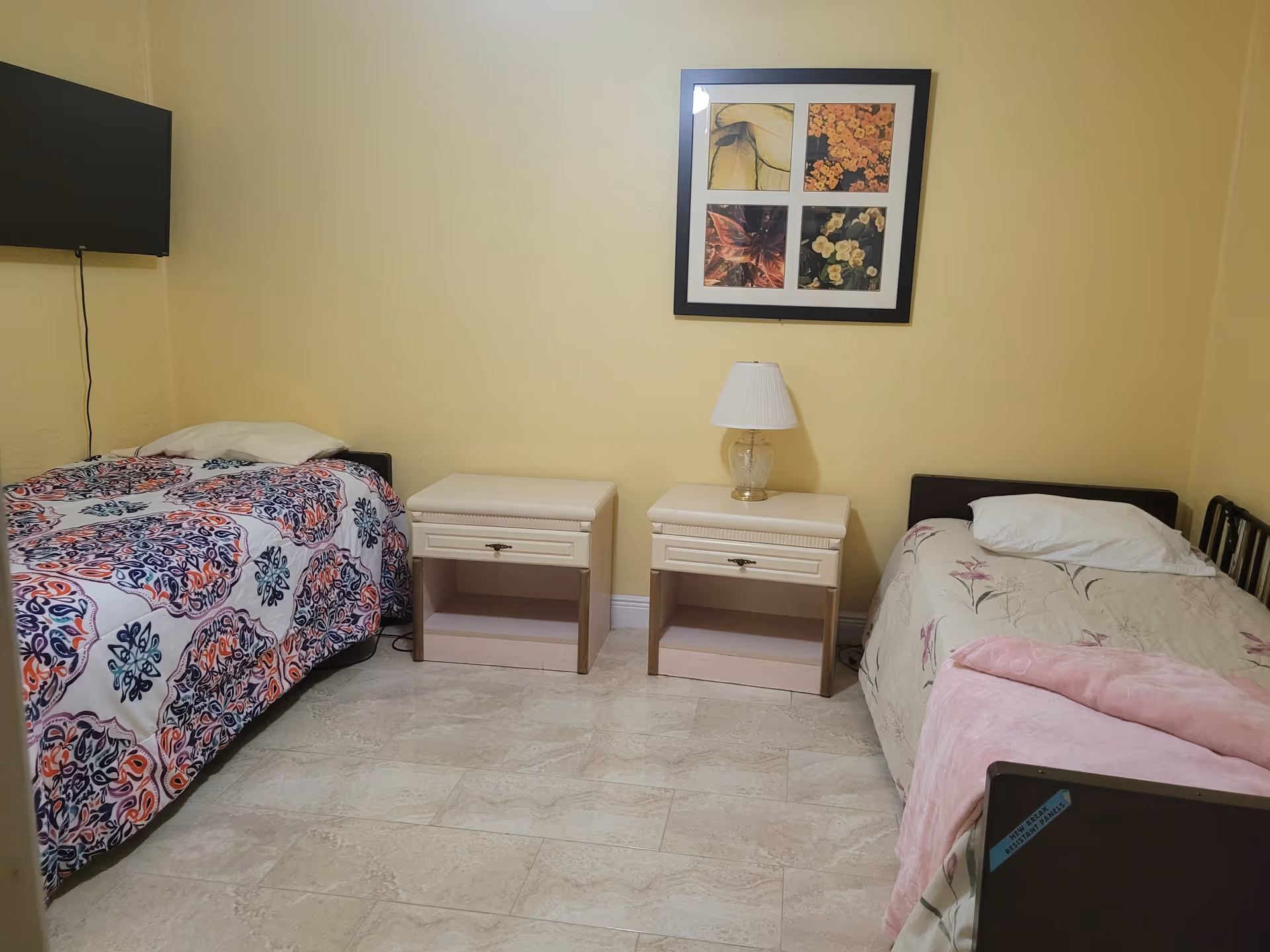 Two single beds with nightstands, lamp, and framed art in a yellow bedroom.