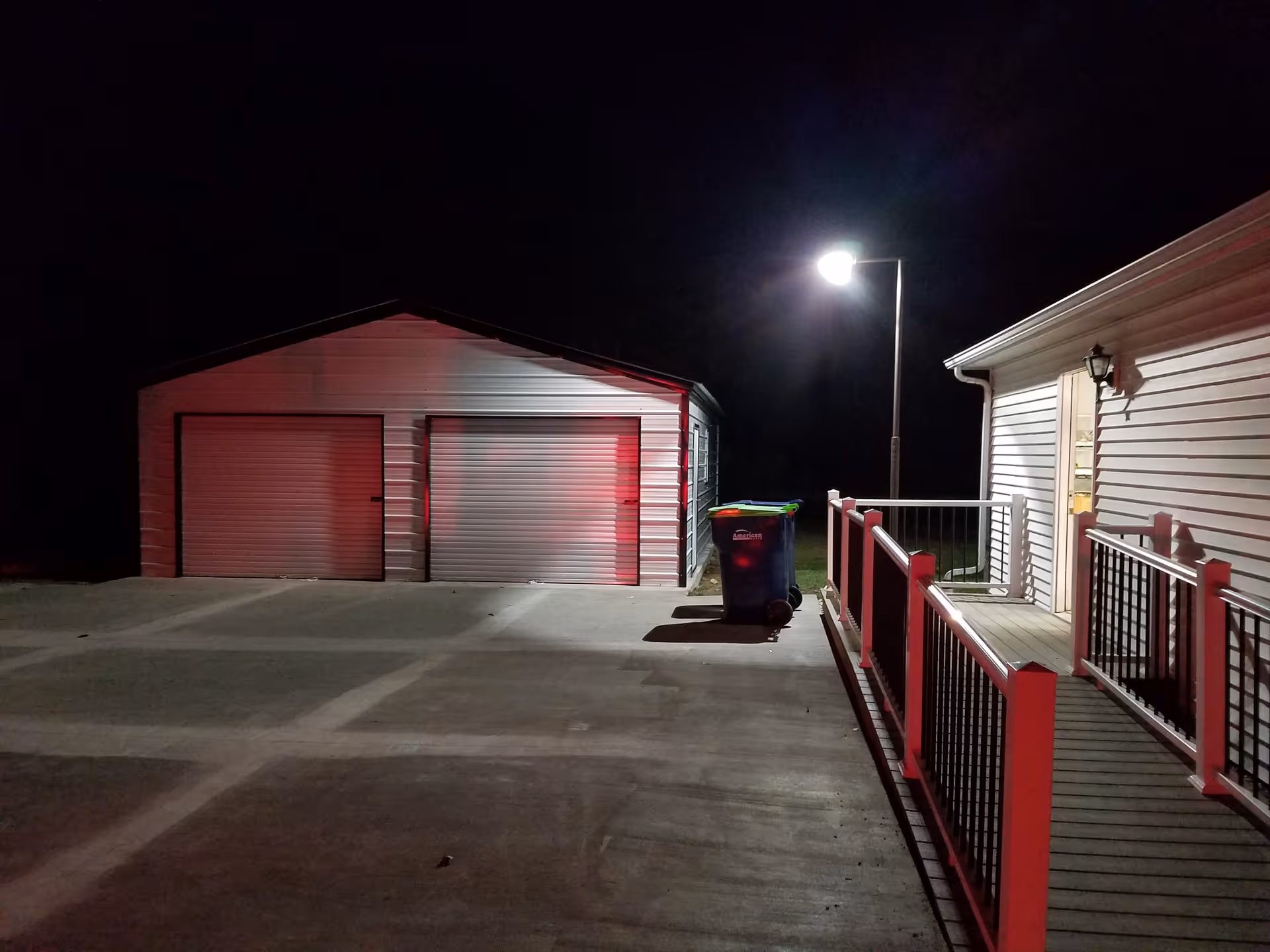 Night exterior view of a building with a ramped walkway, railing, and two garage doors.