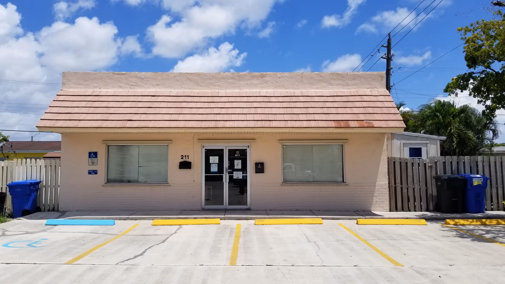 Small beige building with a tiled roof and marked parking spaces in front.