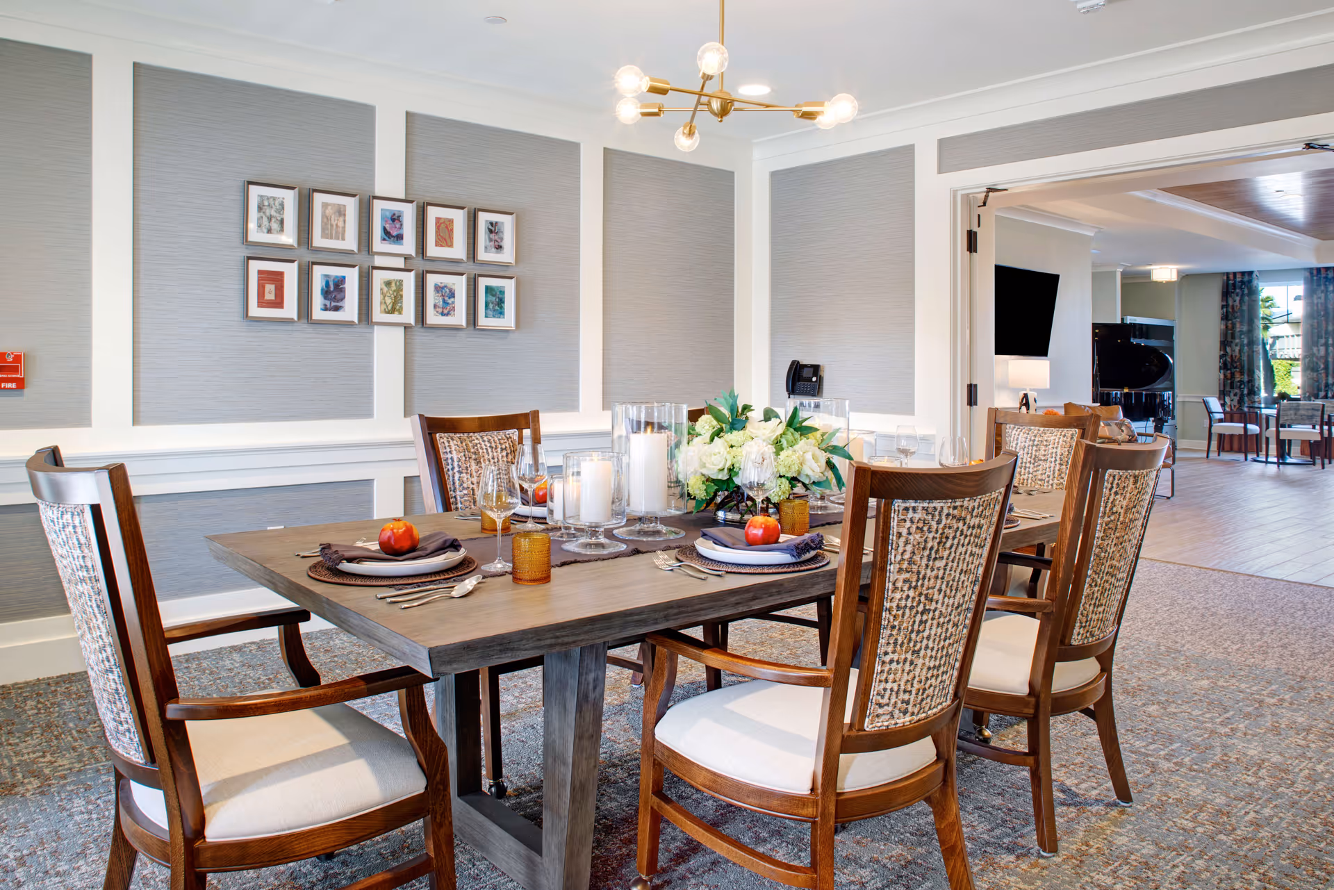 A well-lit dining room with a wooden table, chairs, centerpiece flowers, and candles.