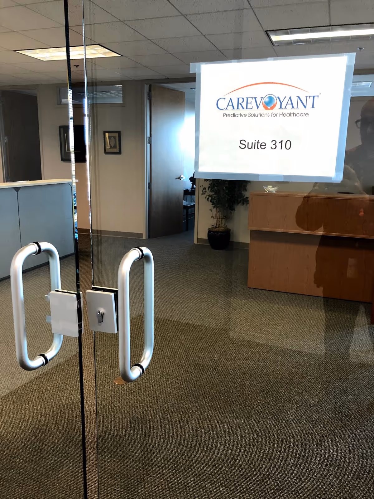 Glass entry with double door handles and a hanging Carevoyant Suite 310 sign.