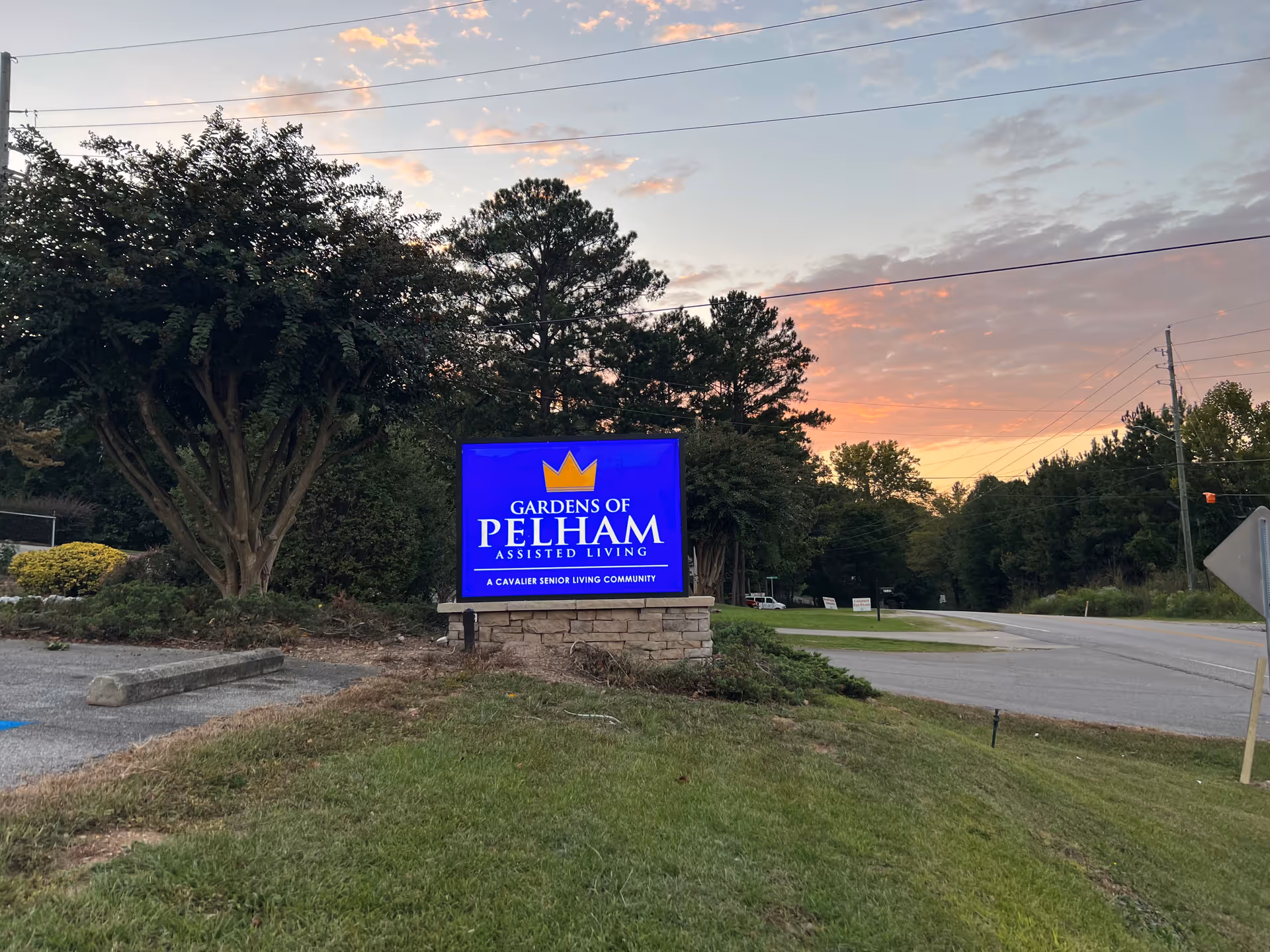 Blue Gardens of Pelham sign on stone base, surrounded by trees and sunset sky.