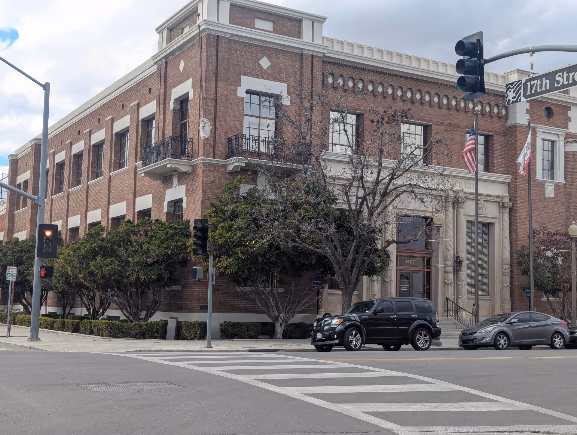 Brick building on a city street corner with trees, traffic lights, and parked cars.