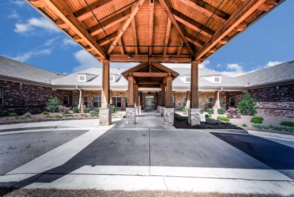 Wooden porte-cochere entrance leads to a brick senior living facility exterior.