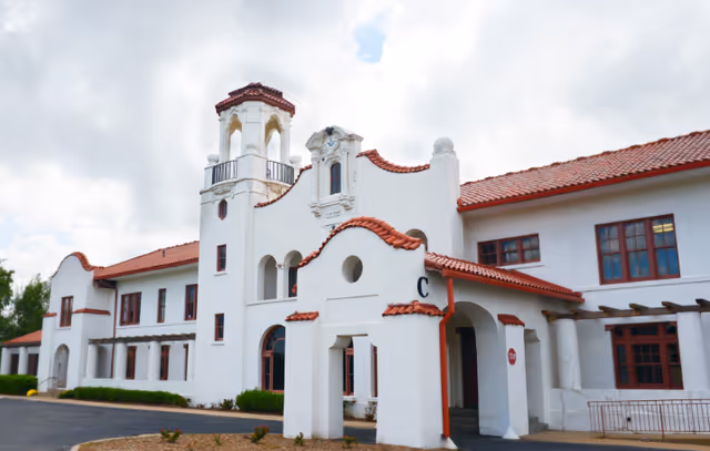 Exterior view of a large white building with red tile roofing and arched architectural details under a partly cloudy sky.