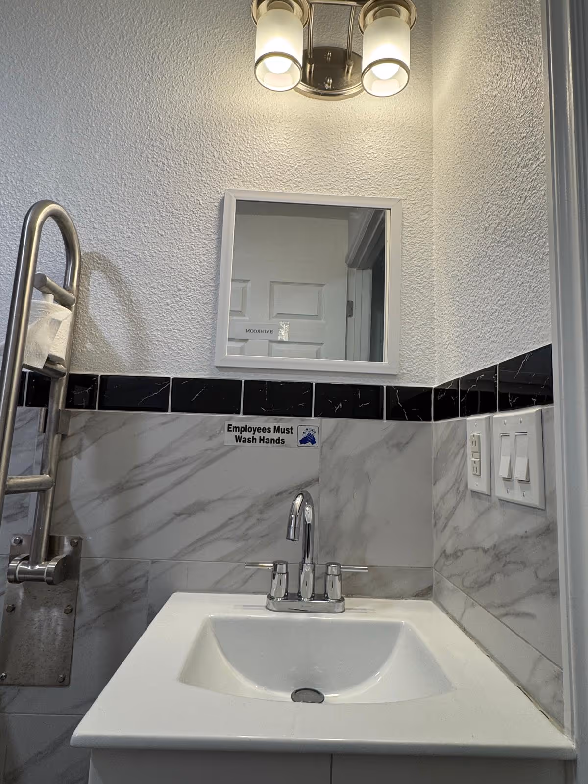 Bathroom sink with mirror and marble-tiled walls, featuring an Employees Must Wash Hands sign.