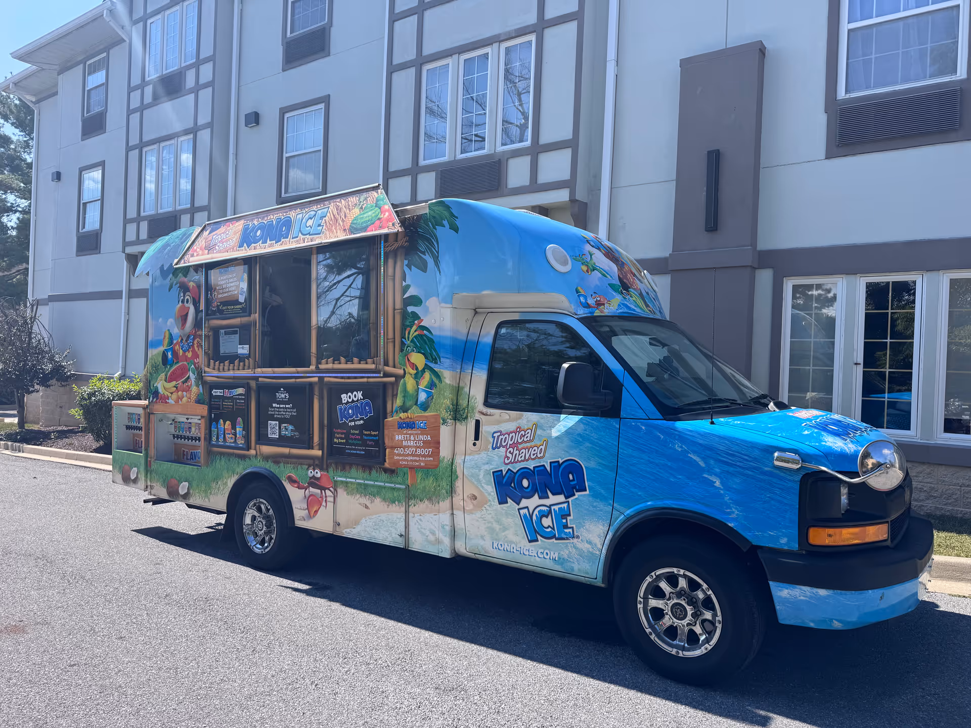 Blue Kona Ice truck parked in front of a senior living building.