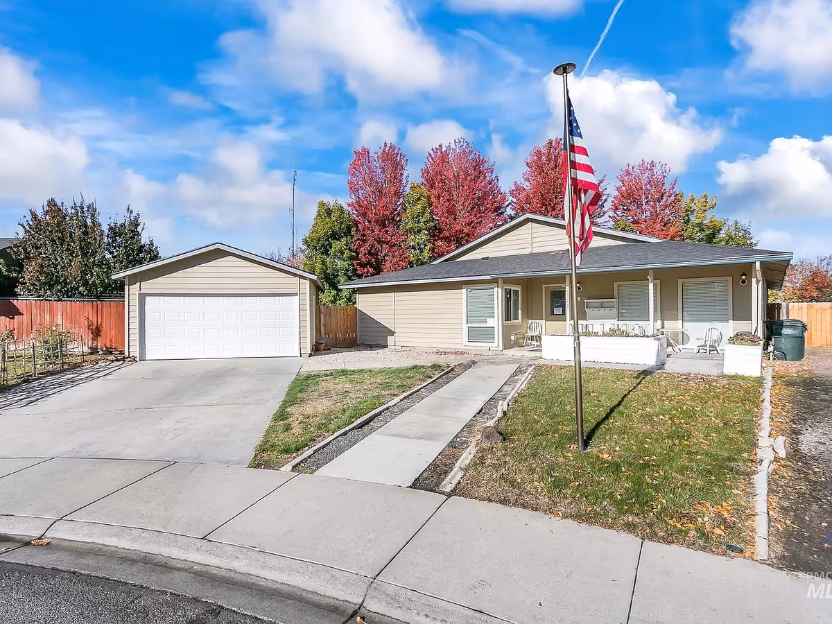 Single-story beige building with attached garage, flagpole, and front porch seating.