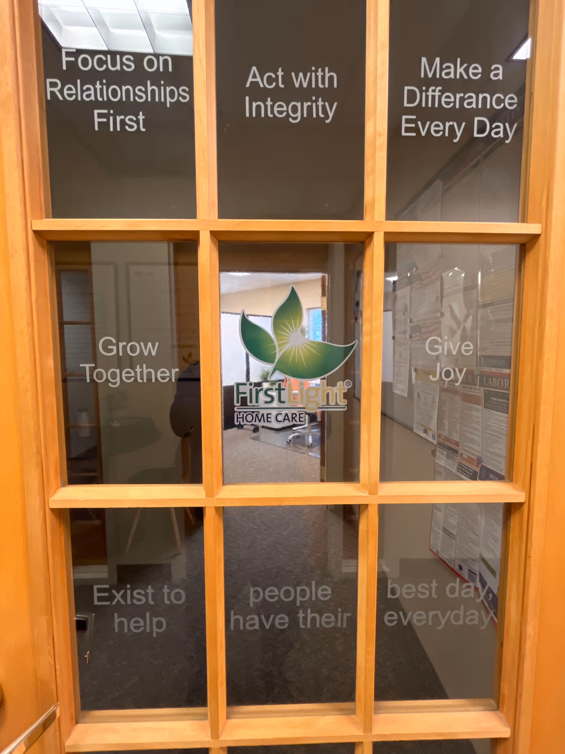 Wood-framed glass door with FirstLight Home Care logo and motivational quotes.