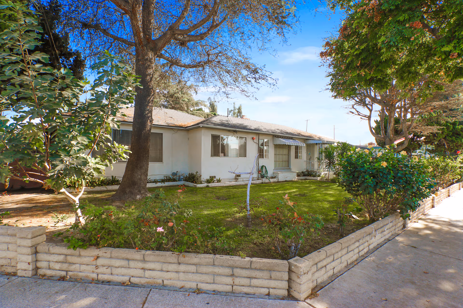 A single-story building with a manicured front yard, trees, and a low brick border.