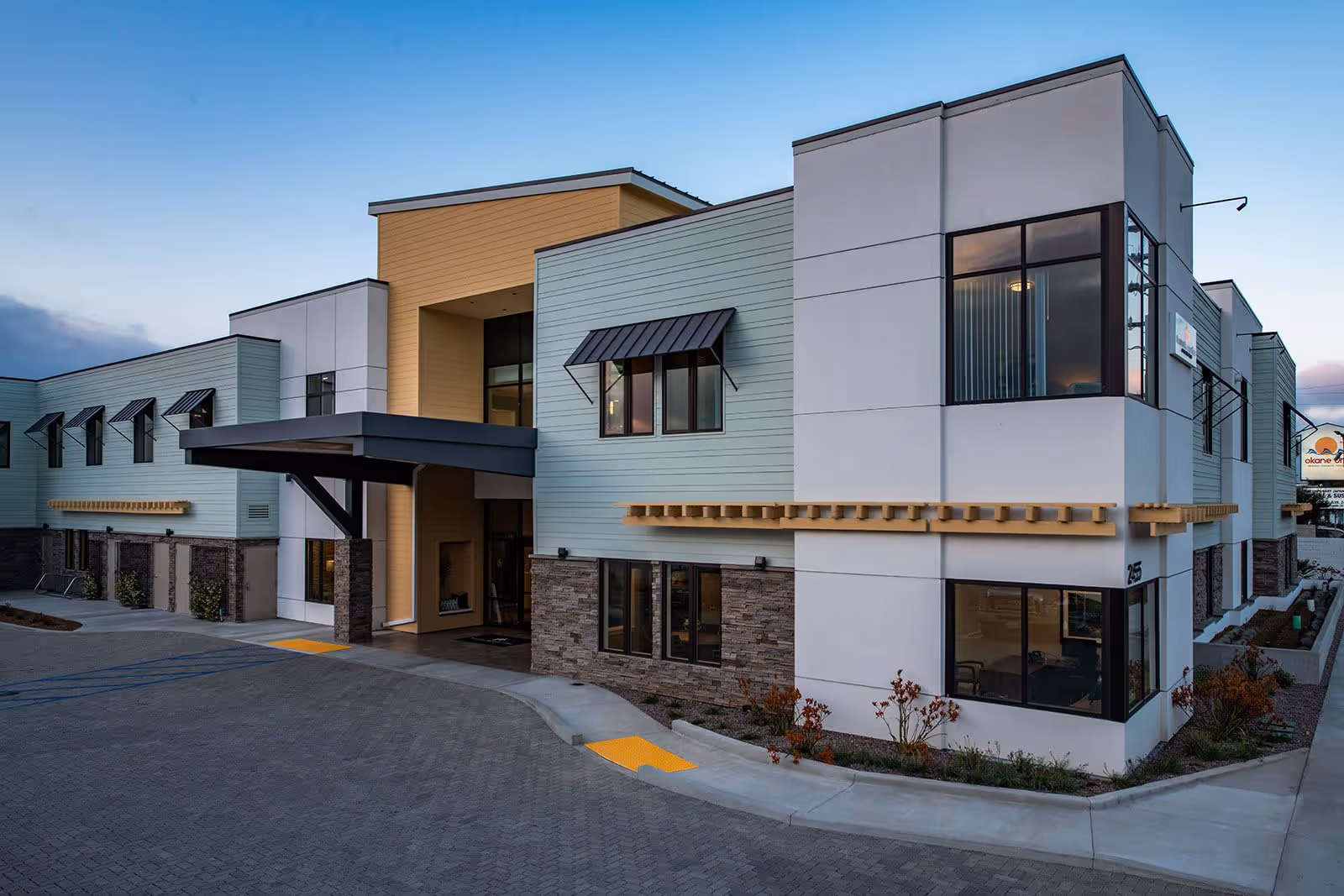 Modern two-story senior living facility exterior with a covered entrance canopy, large windows, and landscaped driveway at dusk.