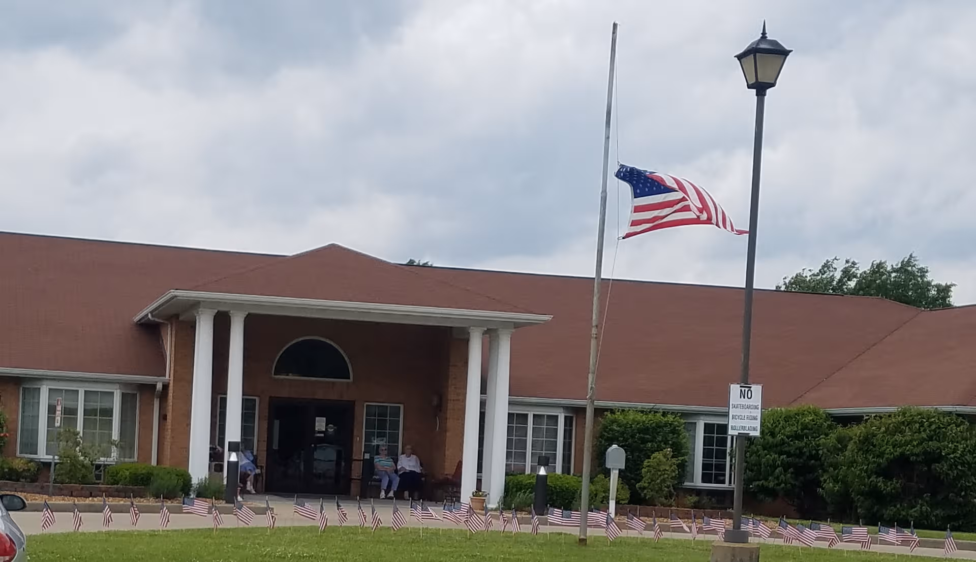 Brick senior living facility with white columns, American flags, and a front entrance.