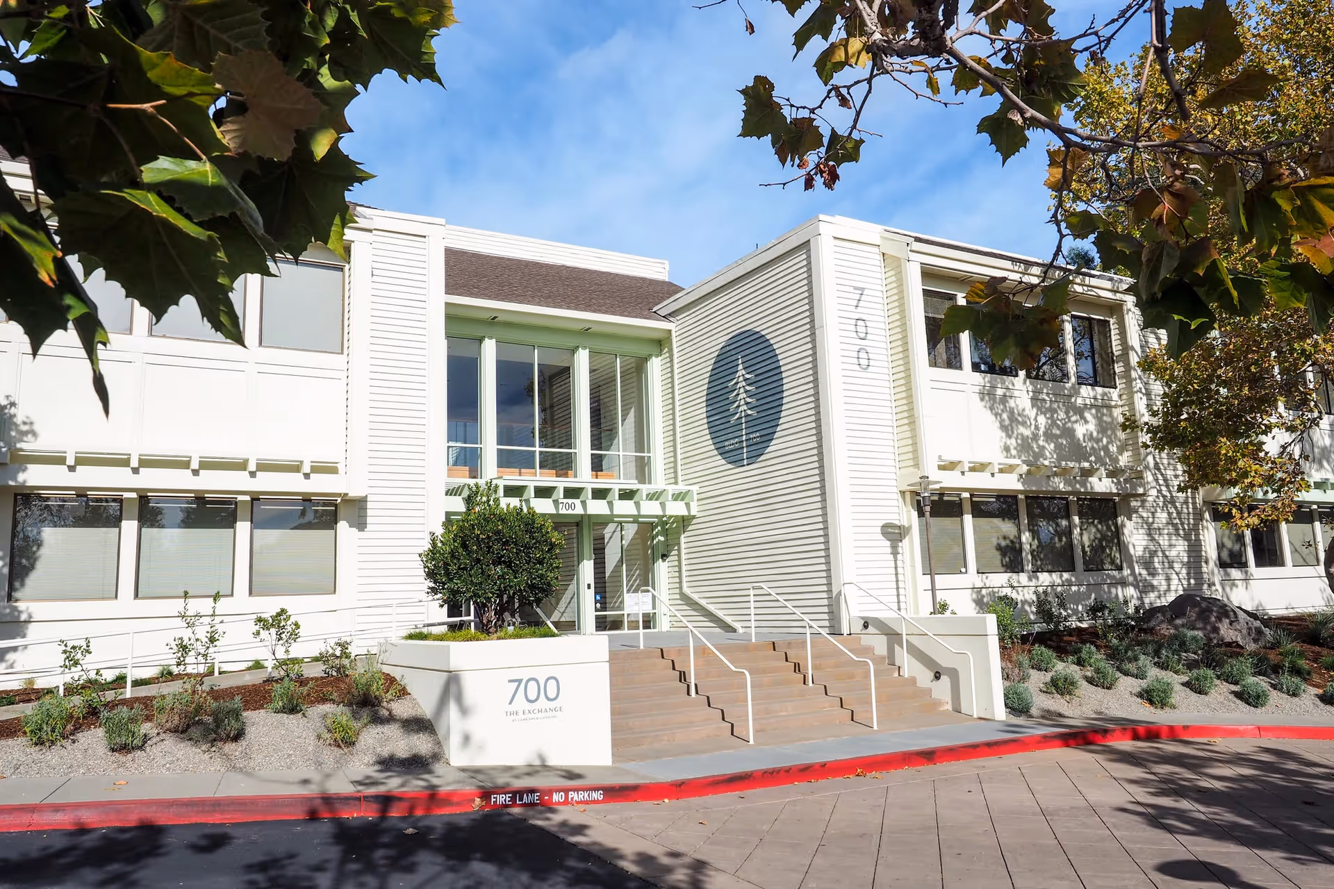 White modern senior living facility exterior with glass entrance, stairs, and landscaped surroundings.
