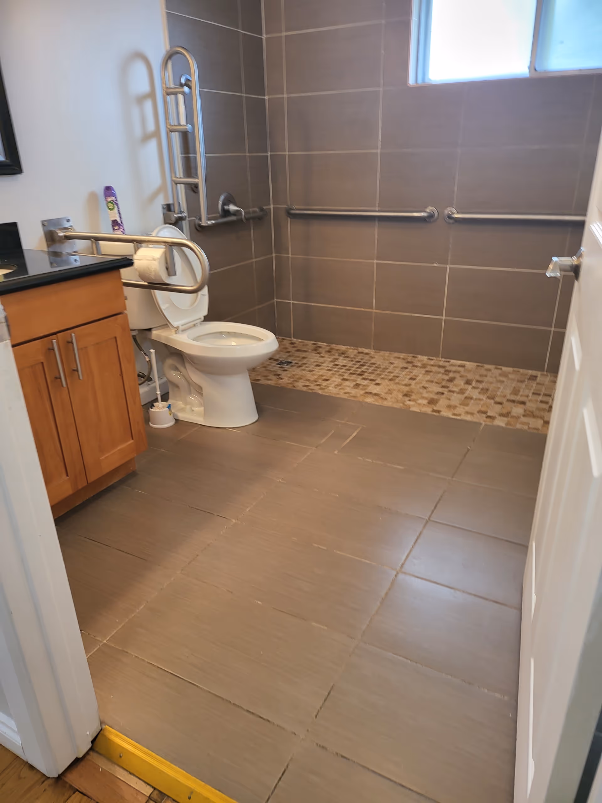 Accessible bathroom with toilet, vanity, and grab bars in a tiled room.