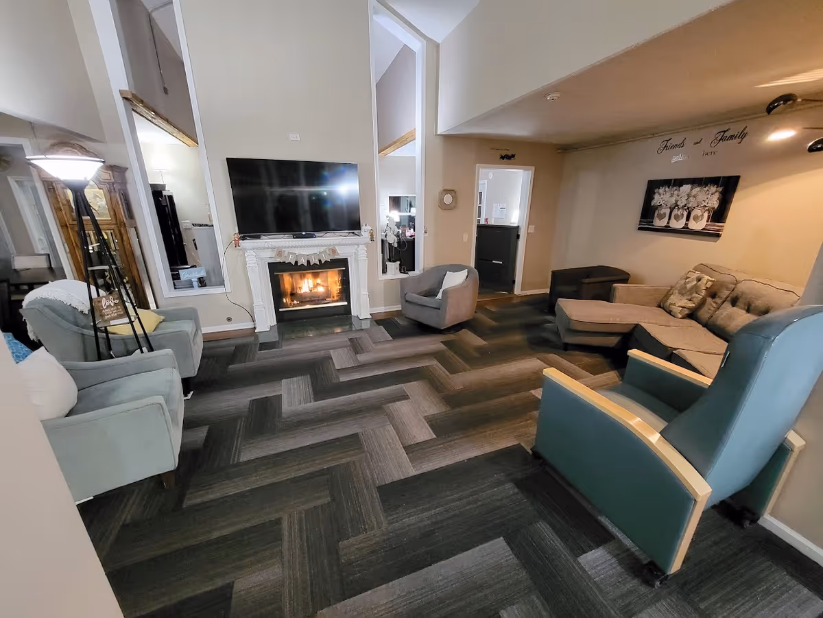 Cozy lounge with fireplace, television, and multiple seating areas in a shared senior living space.
