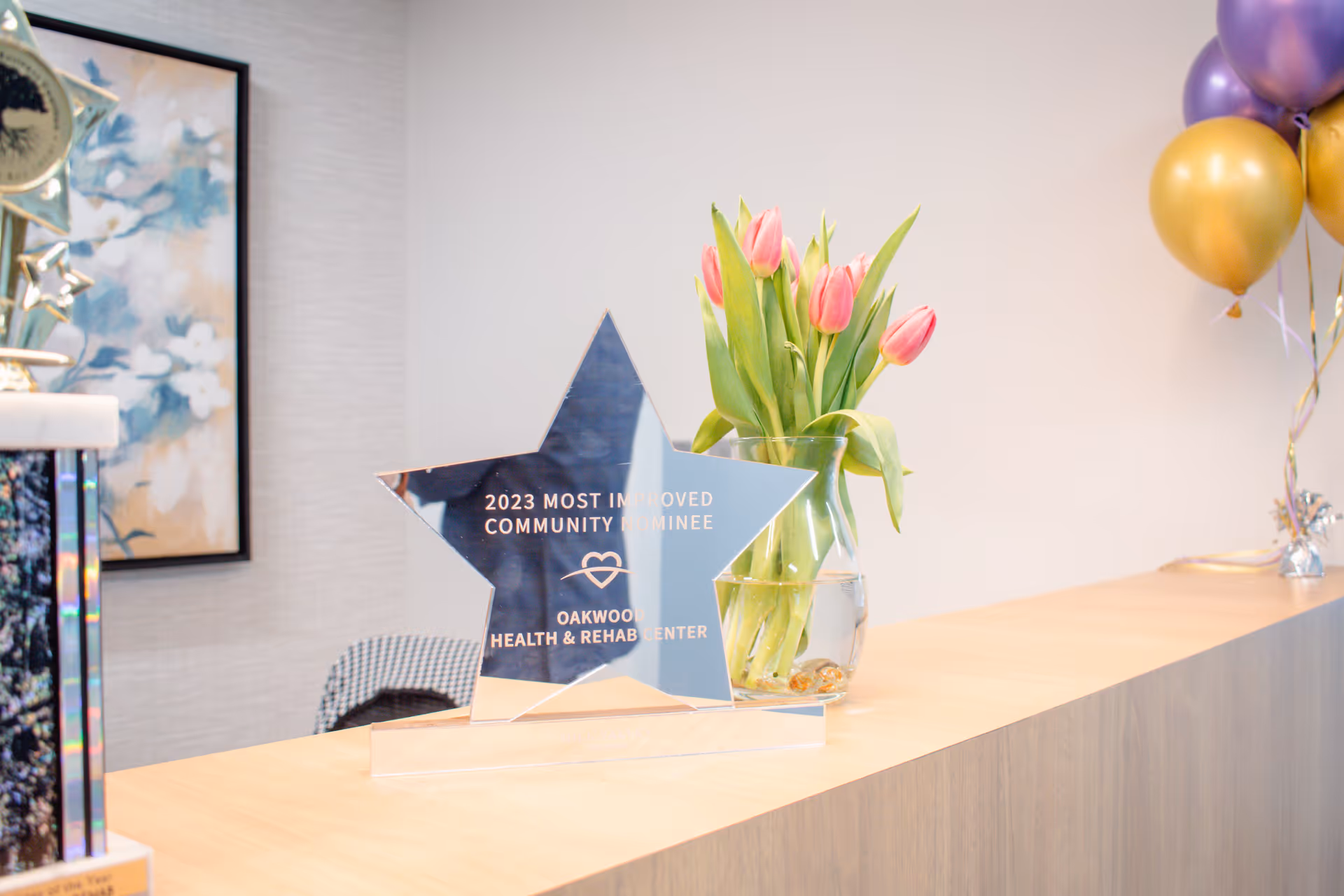Reception counter displaying a star-shaped award, a vase of tulips, and celebratory balloons.