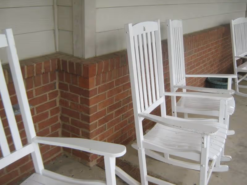 White wooden rocking chairs lined up on a covered brick porch.