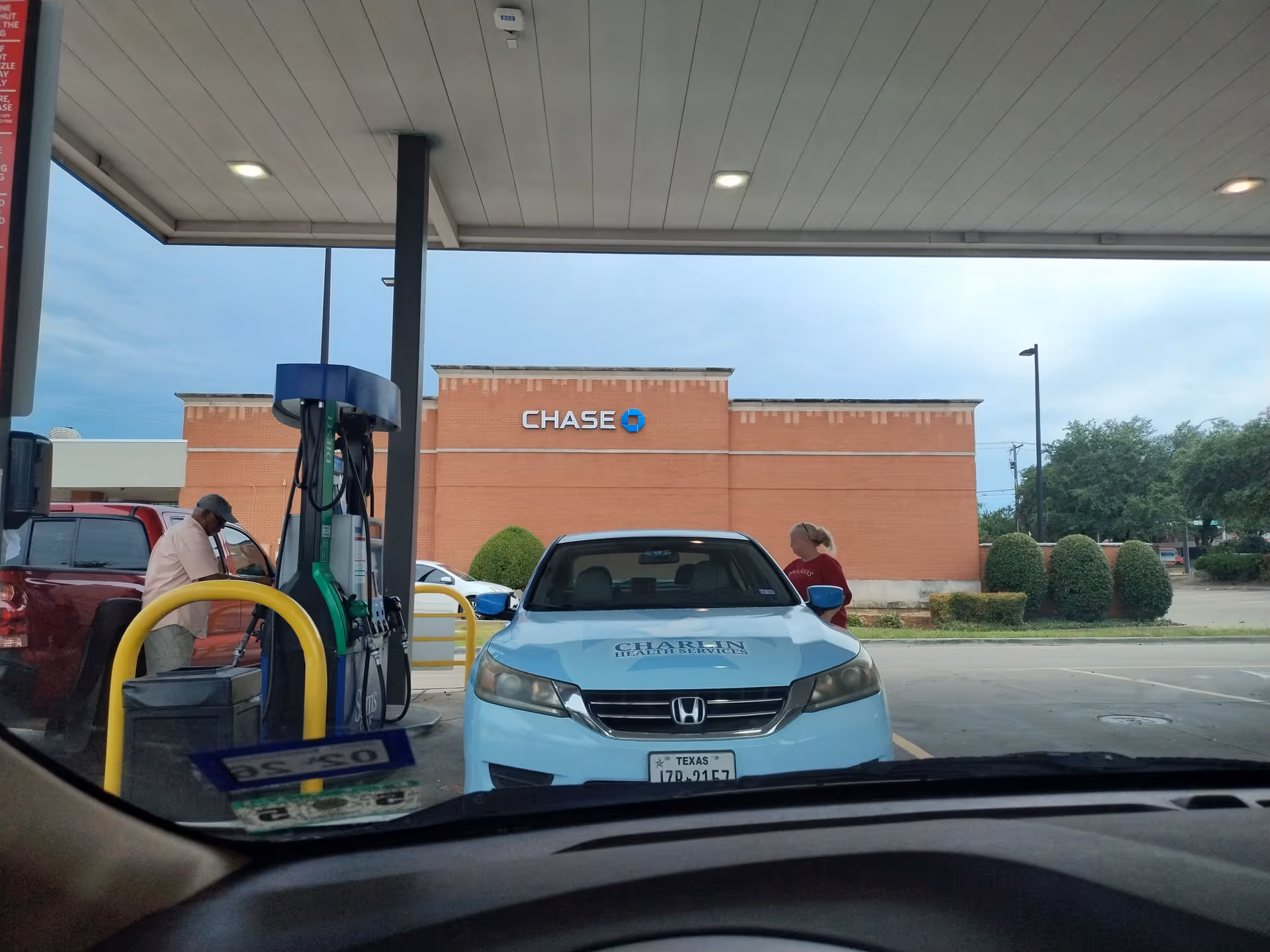 Light-blue car at a gas pump with two people nearby, Charlin Health Services on hood.