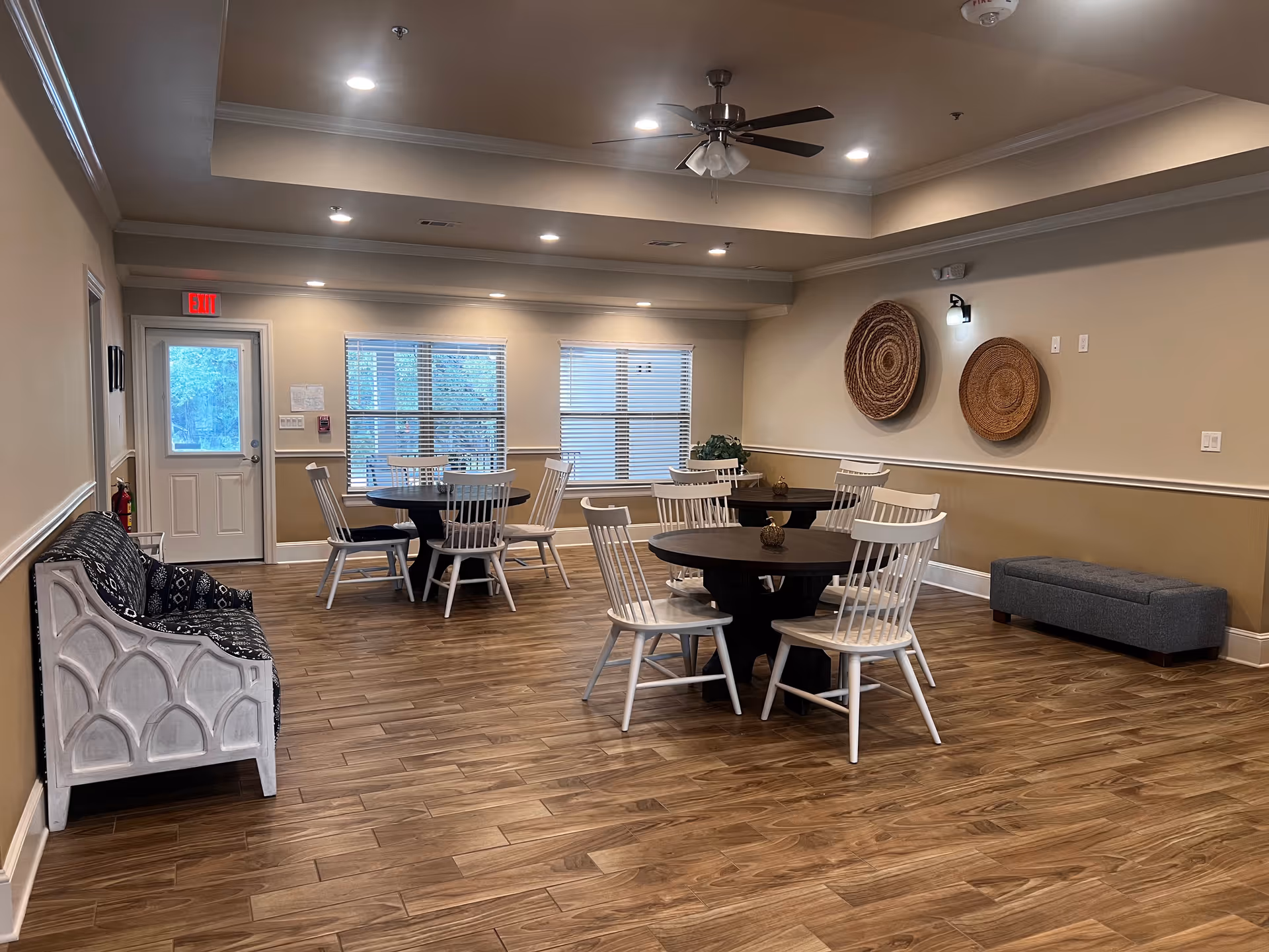 Communal dining area with round tables, white chairs, wooden flooring, and wall decor.