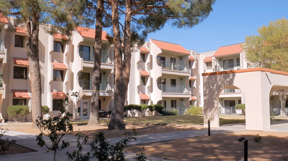 Exterior view of a senior living facility with beige walls, balconies, and trees.