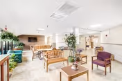 A spacious senior living lounge with seating, plants, and a fireplace.
