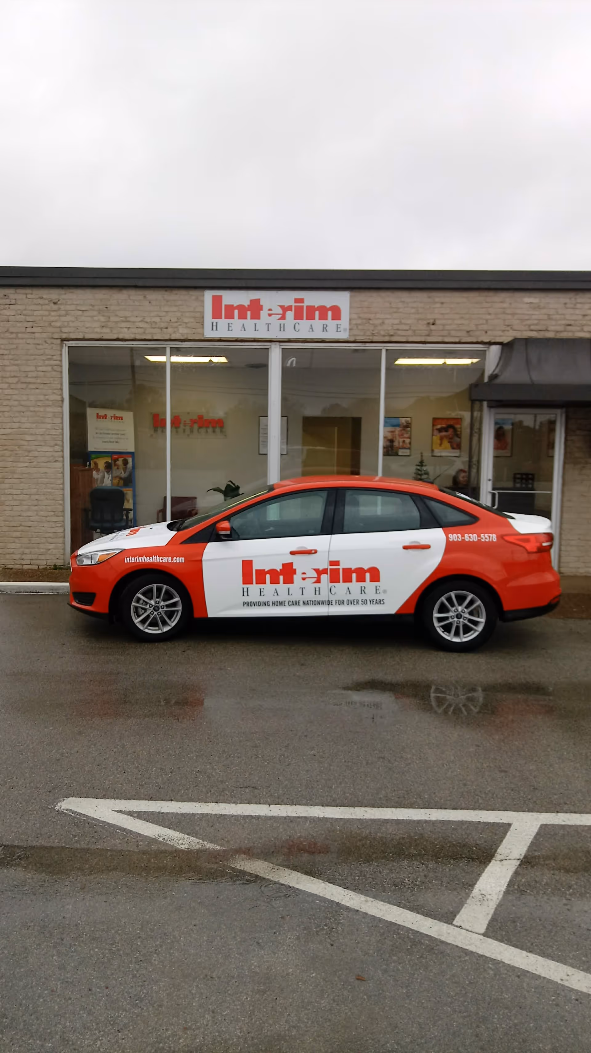 Red and white Interim HealthCare car parked outside a storefront building