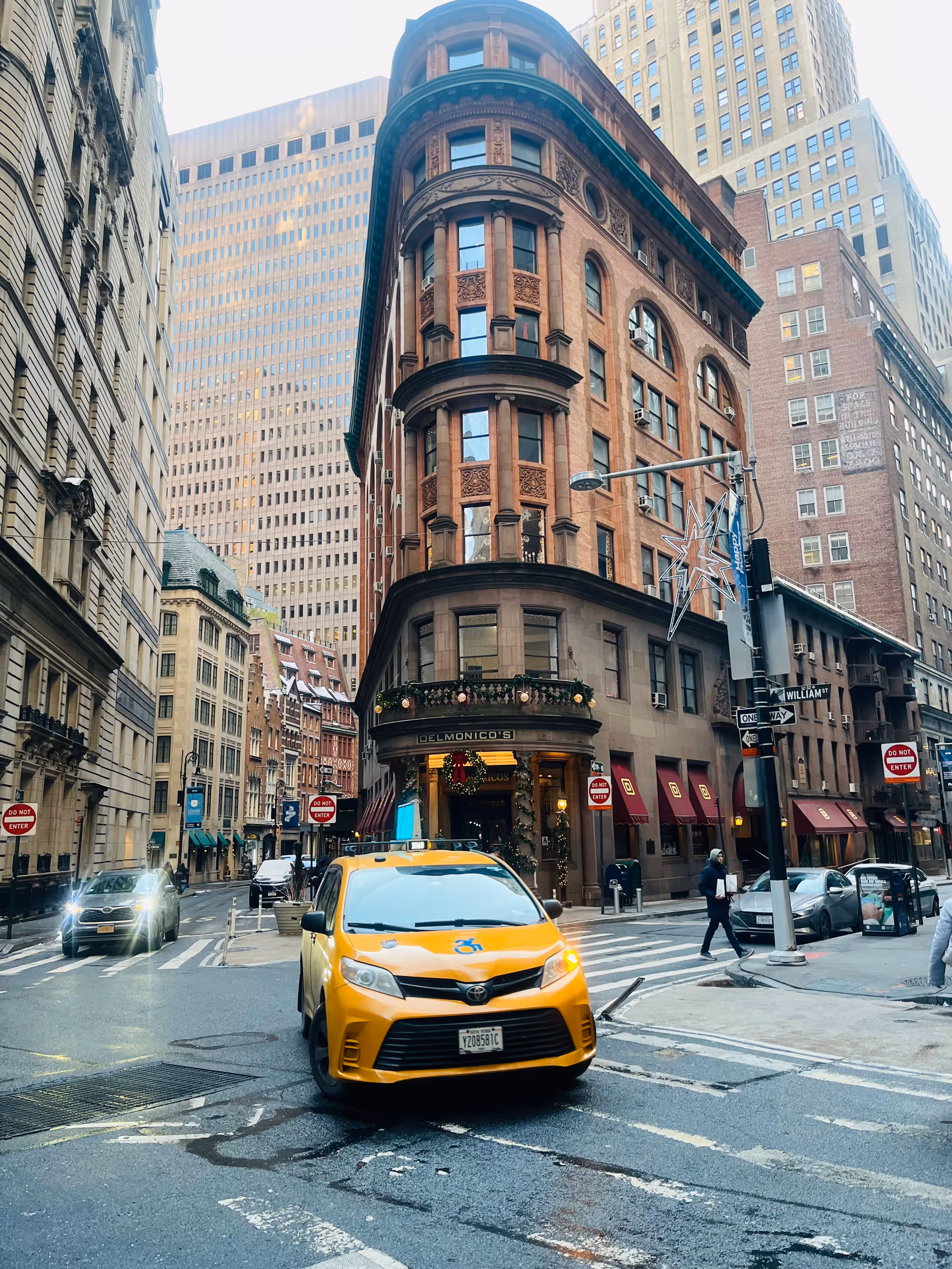 City street with tall brick building, yellow taxi, and Delmonico's storefront below.