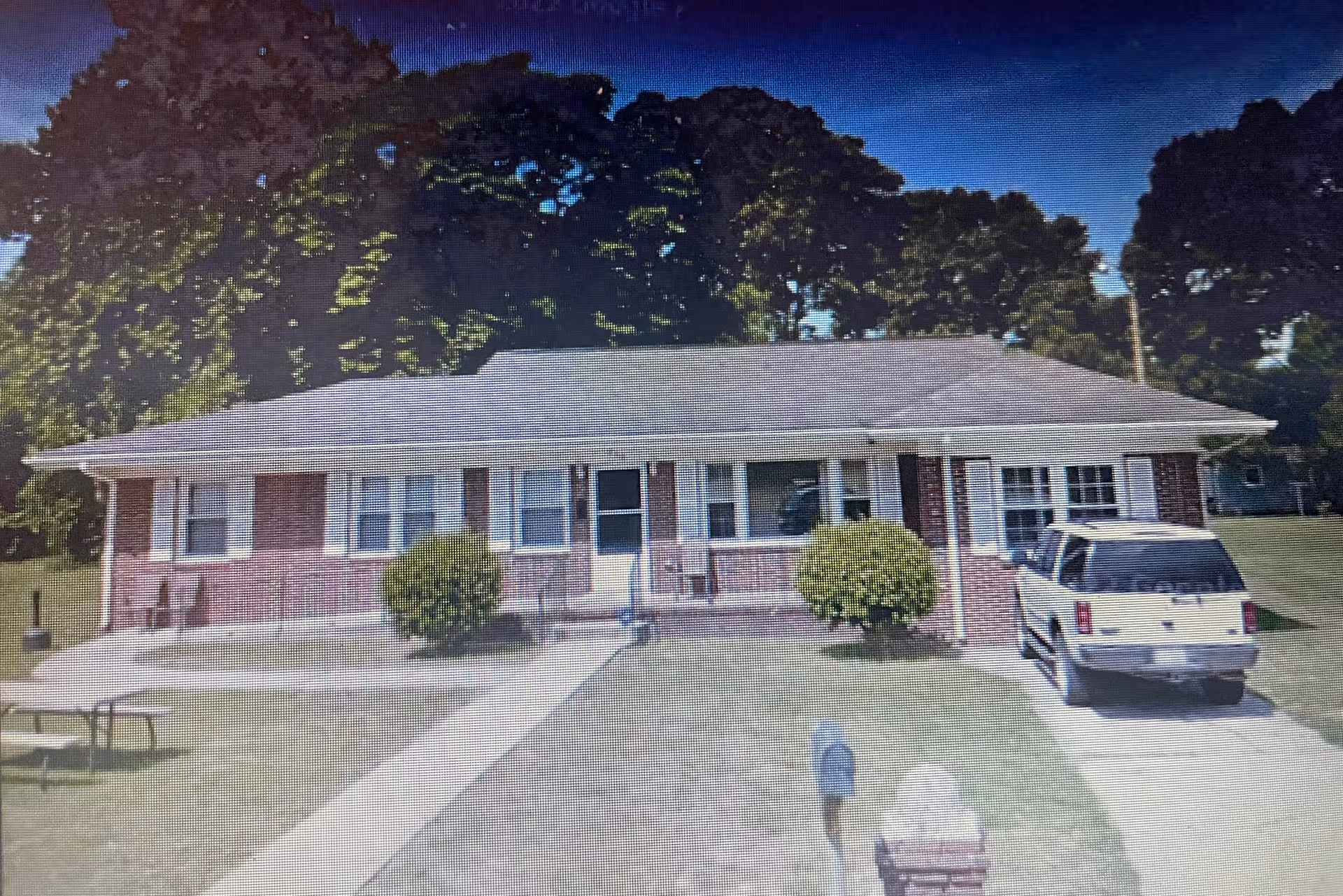 Front exterior of a single-story brick senior living facility with a driveway and parked SUV.