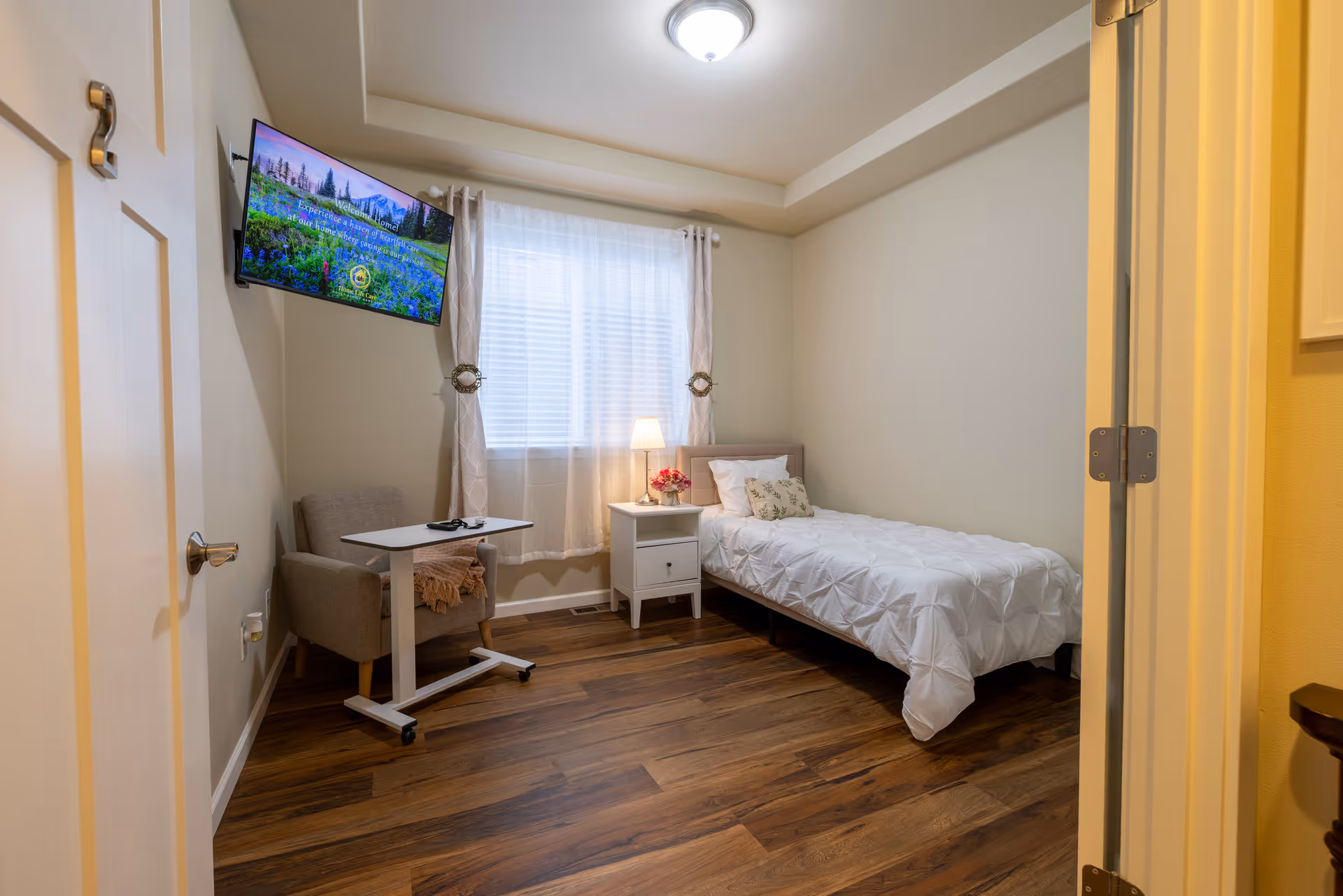 Bedroom in a senior living facility with bed, nightstand, desk, chair, and TV.