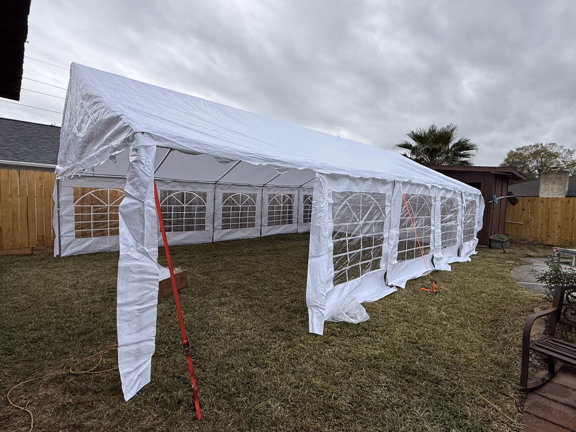 Large white tent set up in a grassy backyard with clear-window side panels.