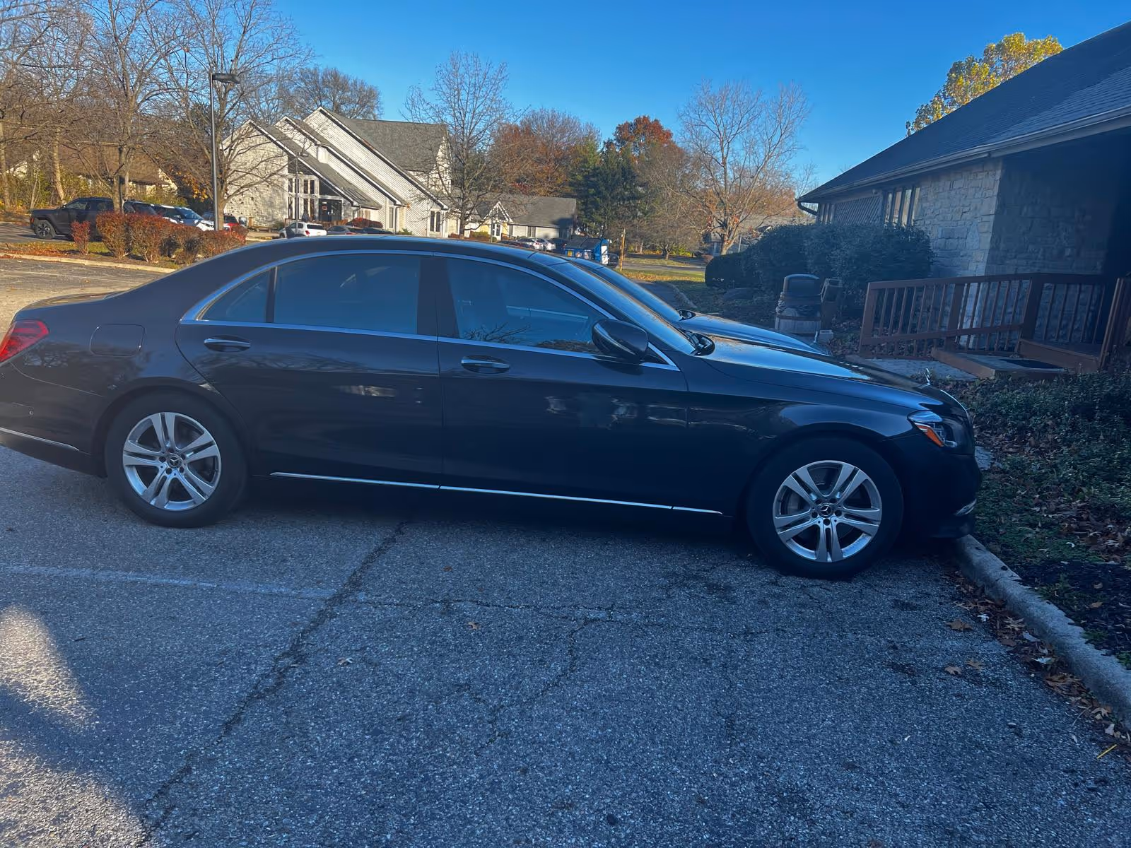 A dark sedan parked in a lot beside a stone building.