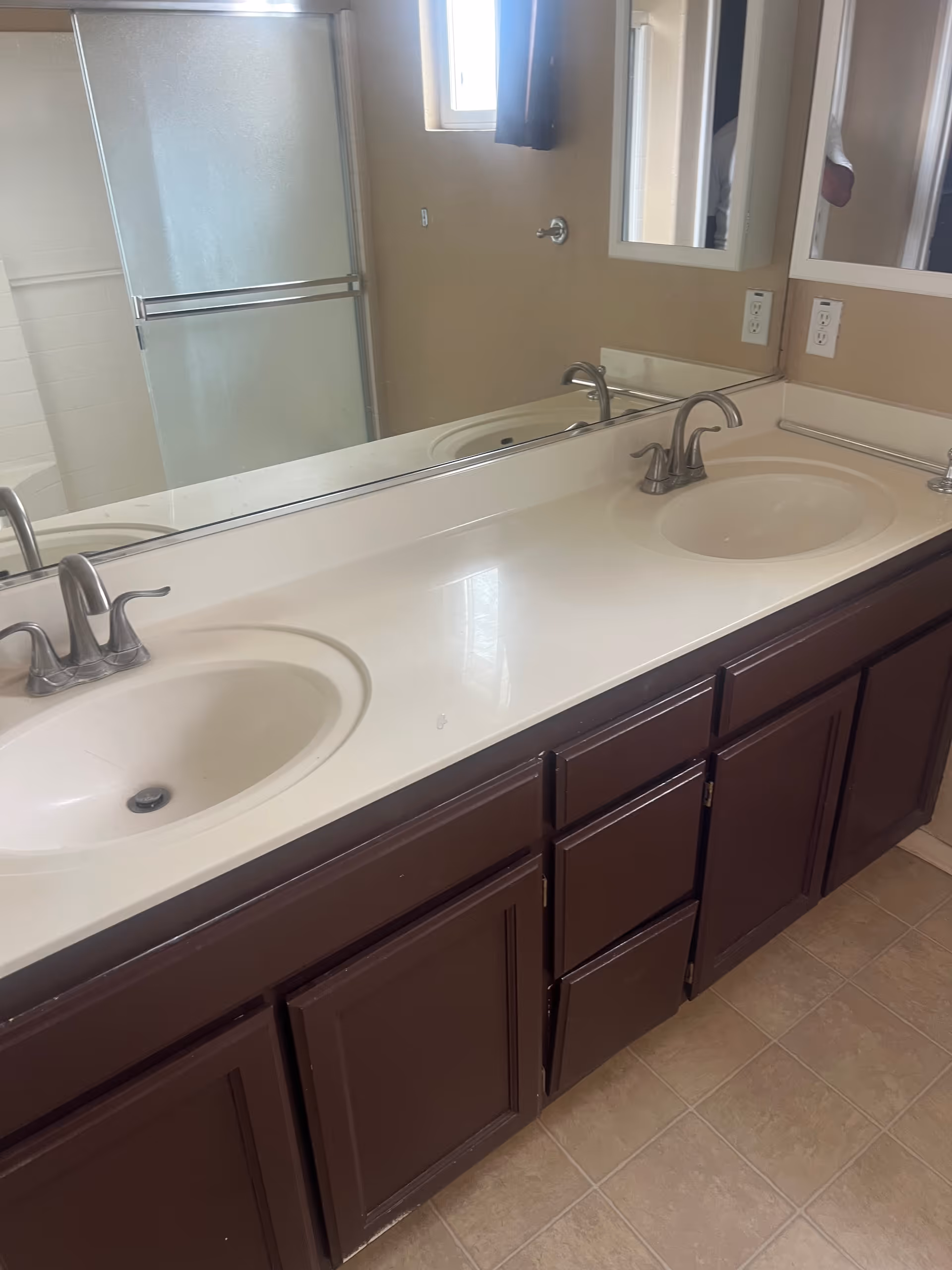 Double sink bathroom vanity with mirrors, cabinets, and a glass shower in the background.