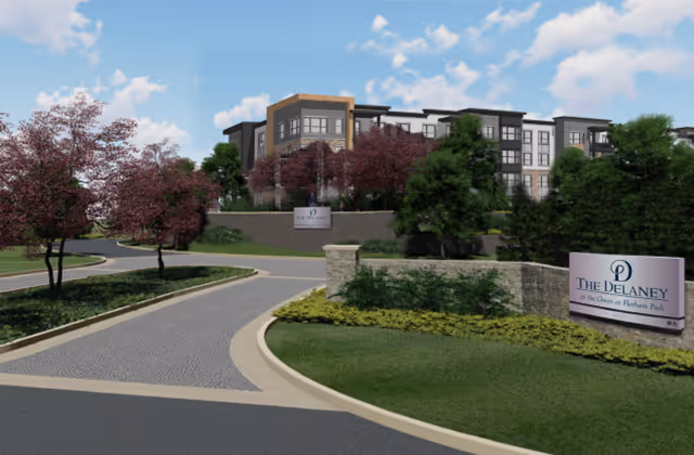 Curved driveway leads to The Delaney at the Green, a modern senior living building with landscaping.