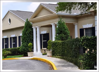 Front exterior of a beige rehabilitation center with columns and manicured hedges.