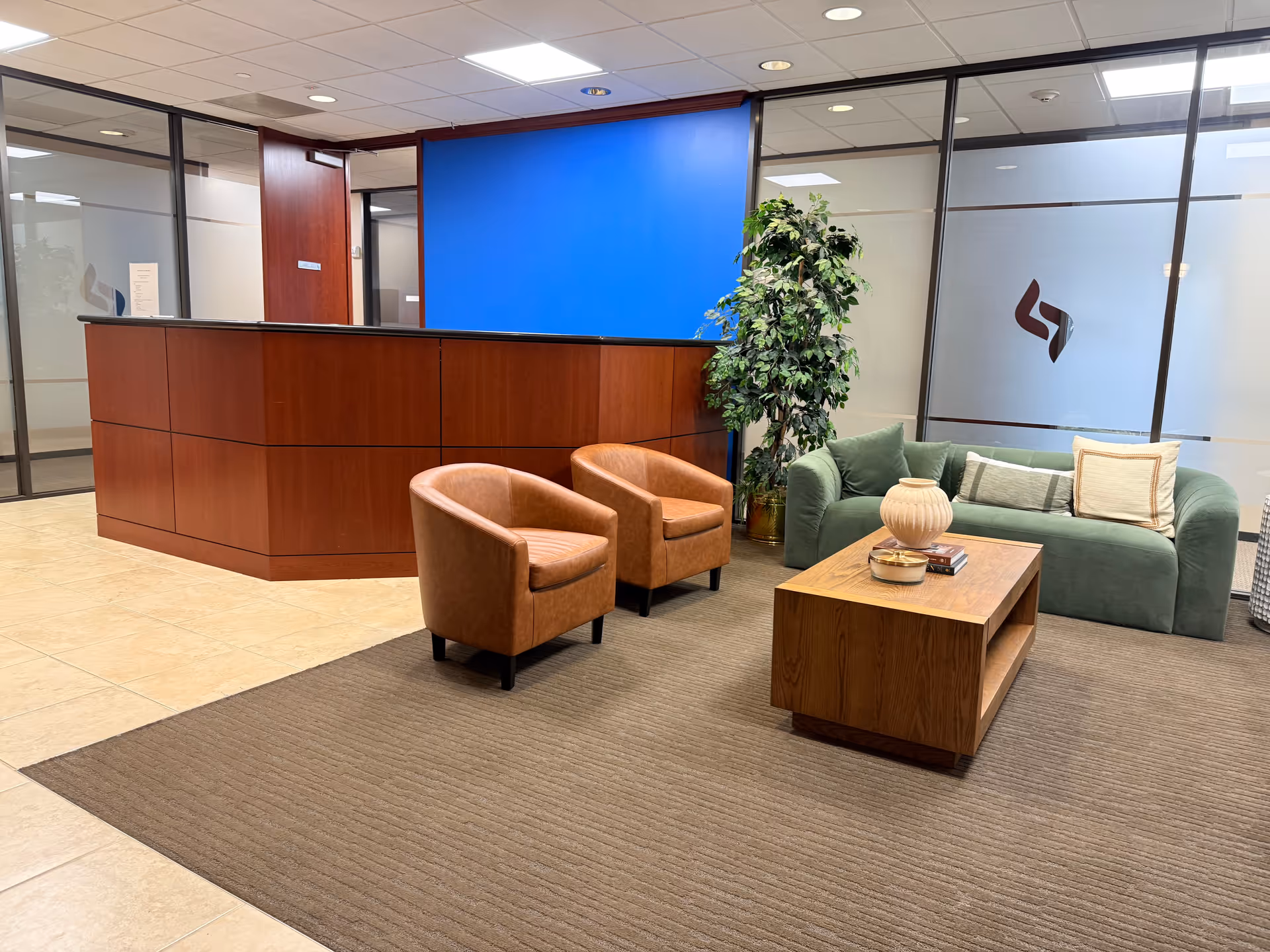 Lobby seating area with brown chairs, green sofa, wooden coffee table, and reception desk.