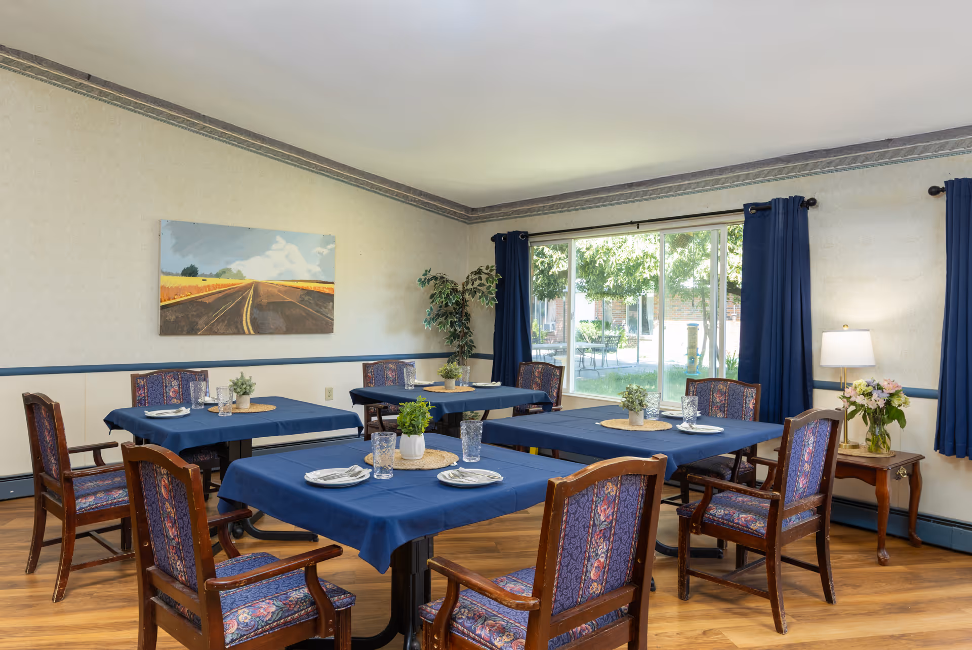 Interior dining room with blue tablecloths, wooden chairs, and a sliding glass door to outdoors.