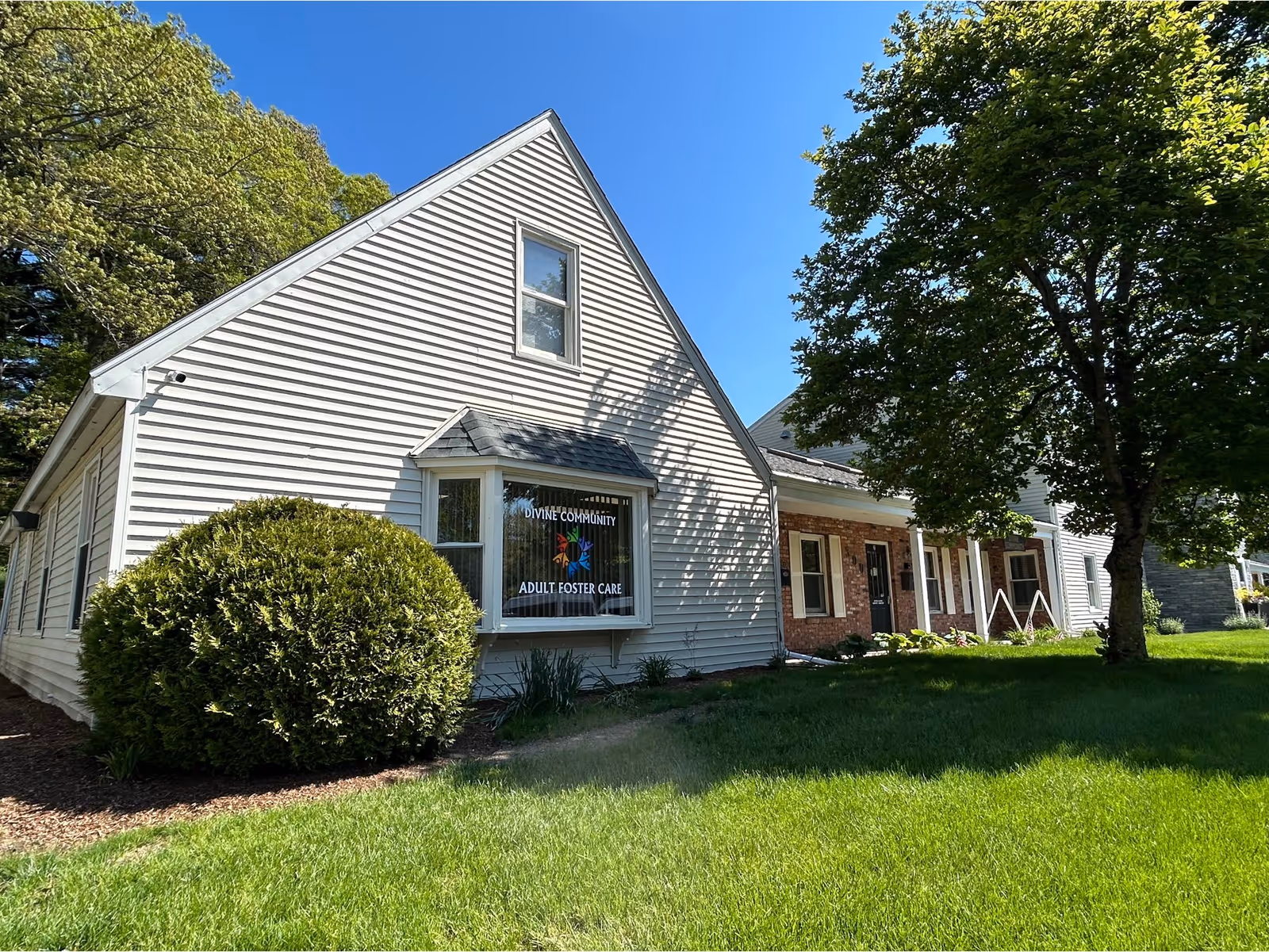 White, gable-roofed building with a storefront window reading Divine Community Adult Foster Care.