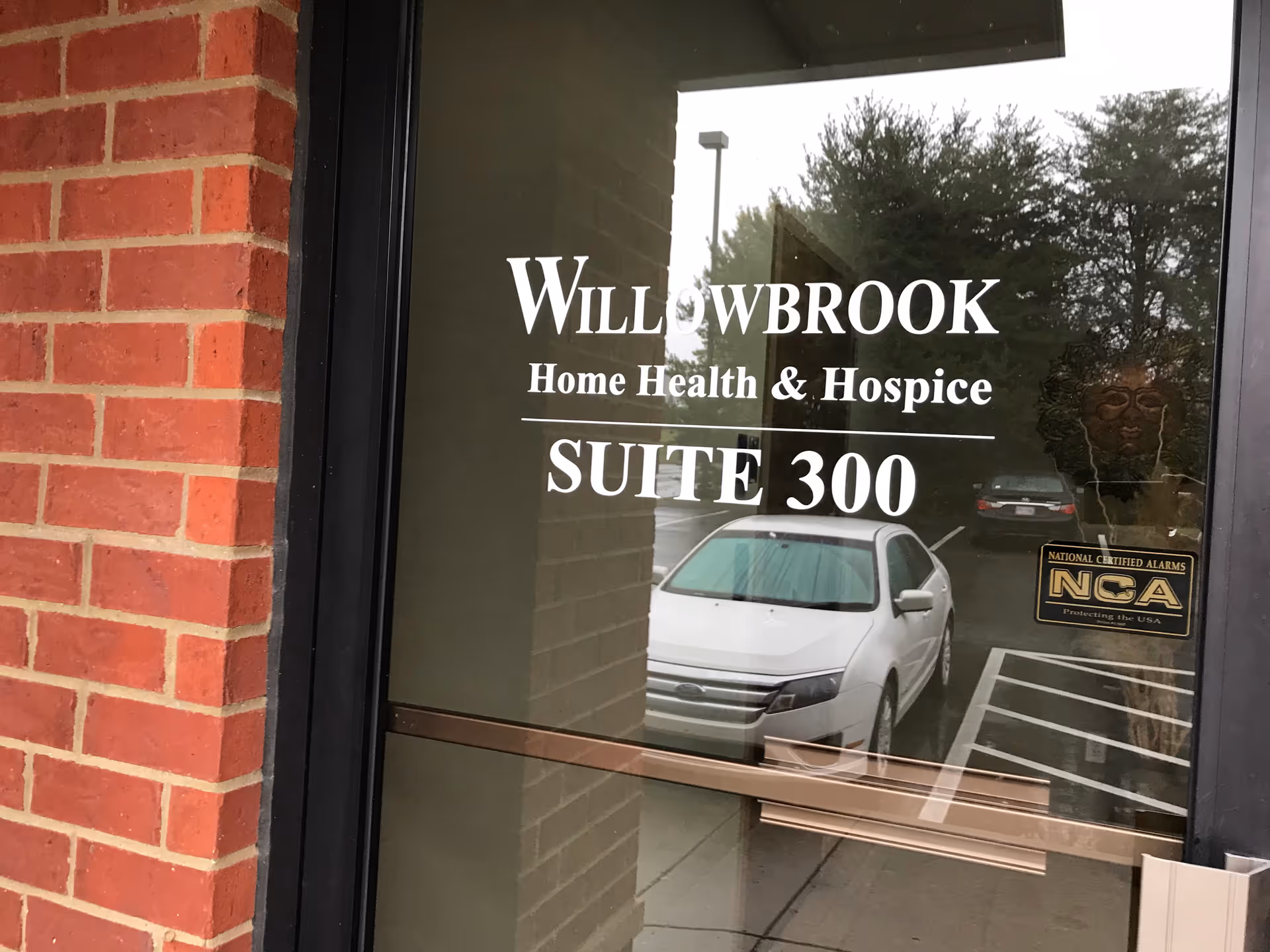 Glass entrance door on brick wall displaying Willowbrook Home Health & Hospice Suite 300