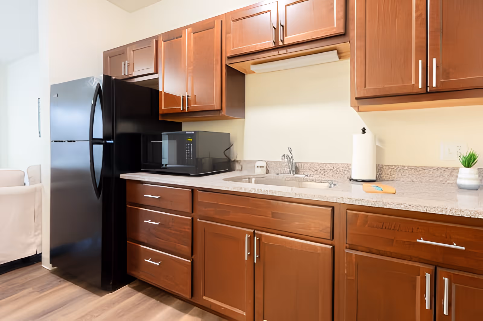 Kitchen with dark wood cabinets, a black refrigerator, microwave, sink and a granite countertop.