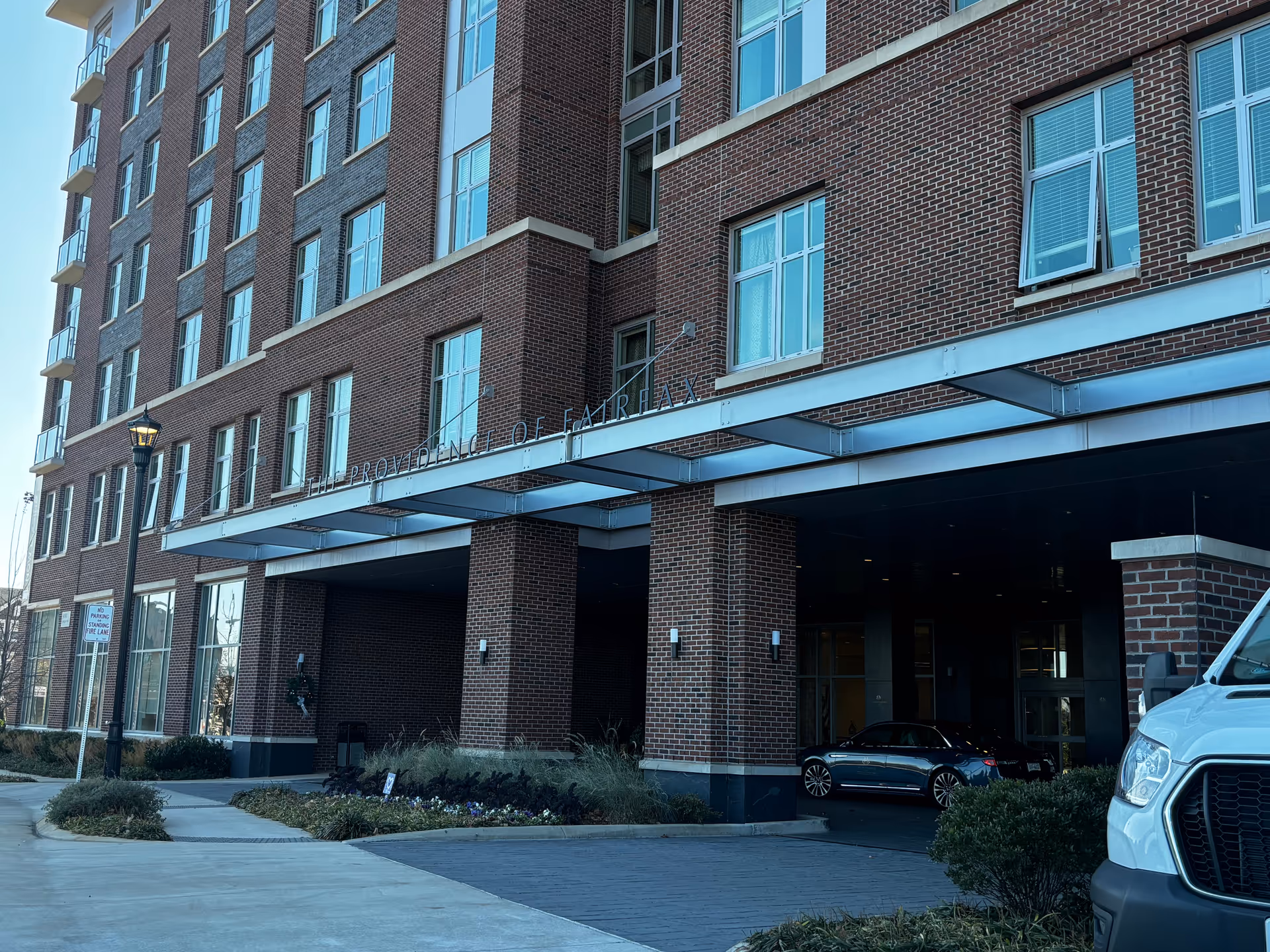 Front view of a multi-story brick building showing the covered entrance canopy and signage reading 'The Providence of Fairfax'.